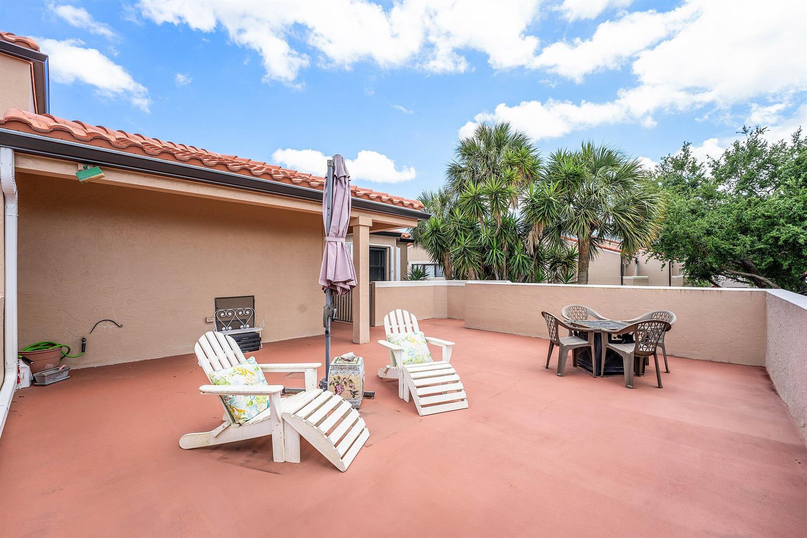 A rooftop patio features white lounge chairs, a dining set, and an umbrella under a sky — 6614 Villa Sonrisa Drive # 123, Boca Raton FL 33433, BOCA RATON, FL
