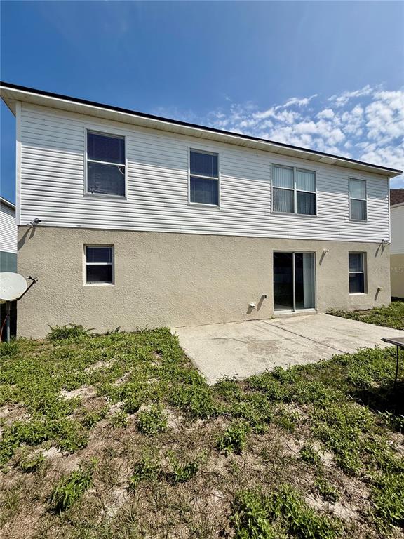The rear exterior of a two-story house features white siding, stucco walls, and a patio — 5445 CHANDLER DRIVE, WINTER HAVEN, FL