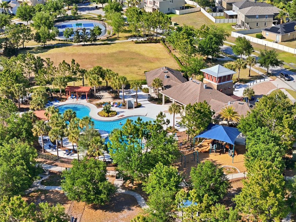 An aerial view shows a community pool, clubhouse, playground, and tennis court surrounded by trees — 7323 LUMBER PORT DRIVE, RUSKIN, FL