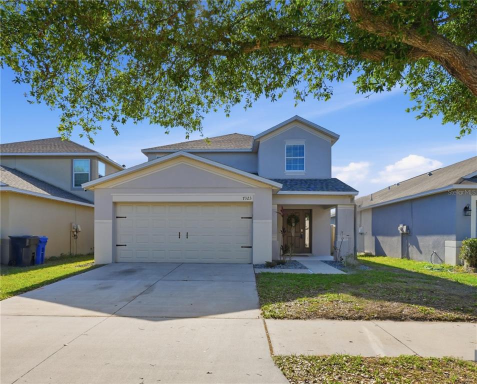 A two-story suburban house with a beige garage, gray siding, and a concrete driveway — 7323 LUMBER PORT DRIVE, RUSKIN, FL