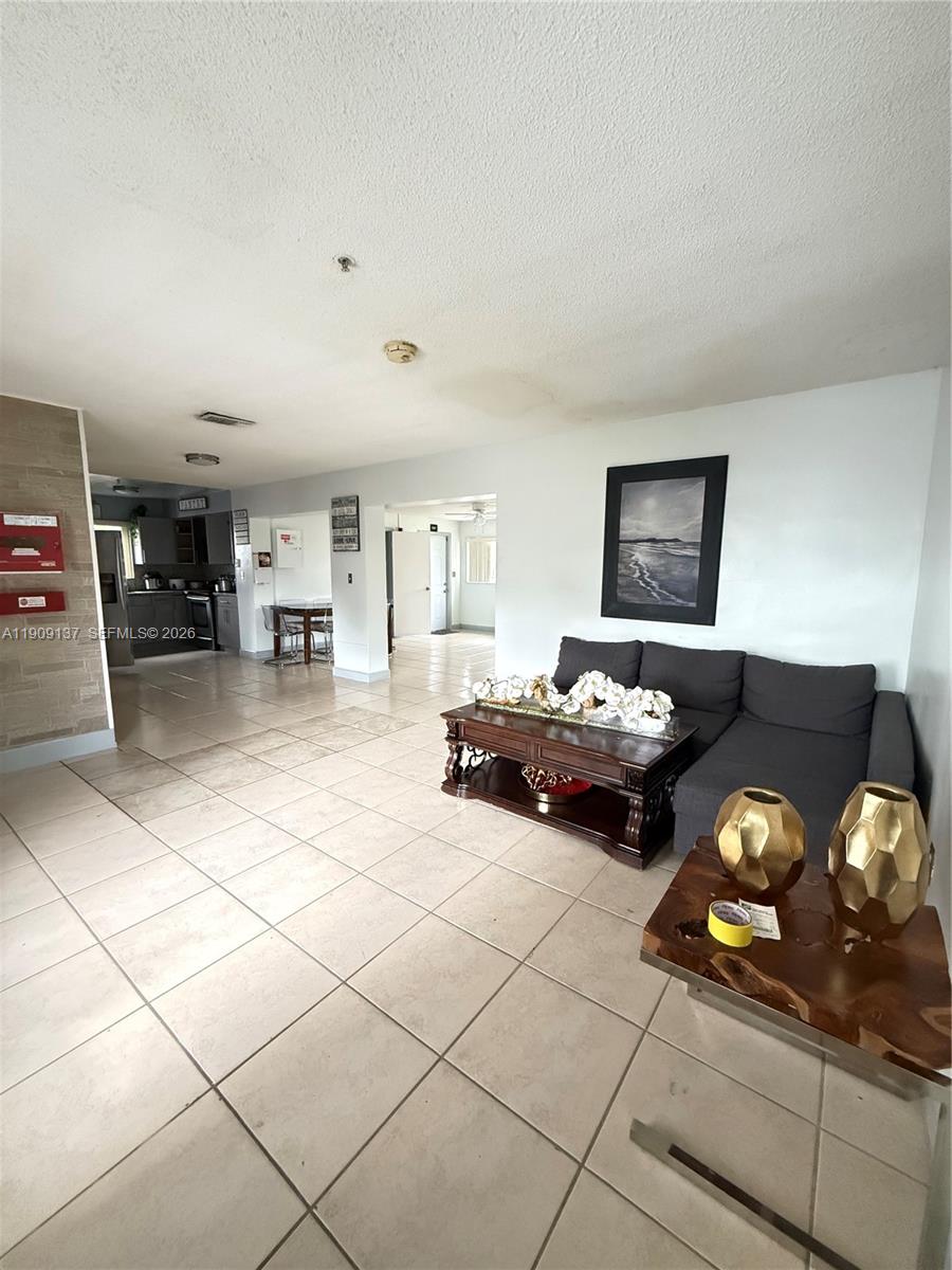A living room with tile flooring, a dark sofa, and a view into the kitchen — 17902 NW 81st Ct, Hialeah FL 33015, HIALEAH, FL