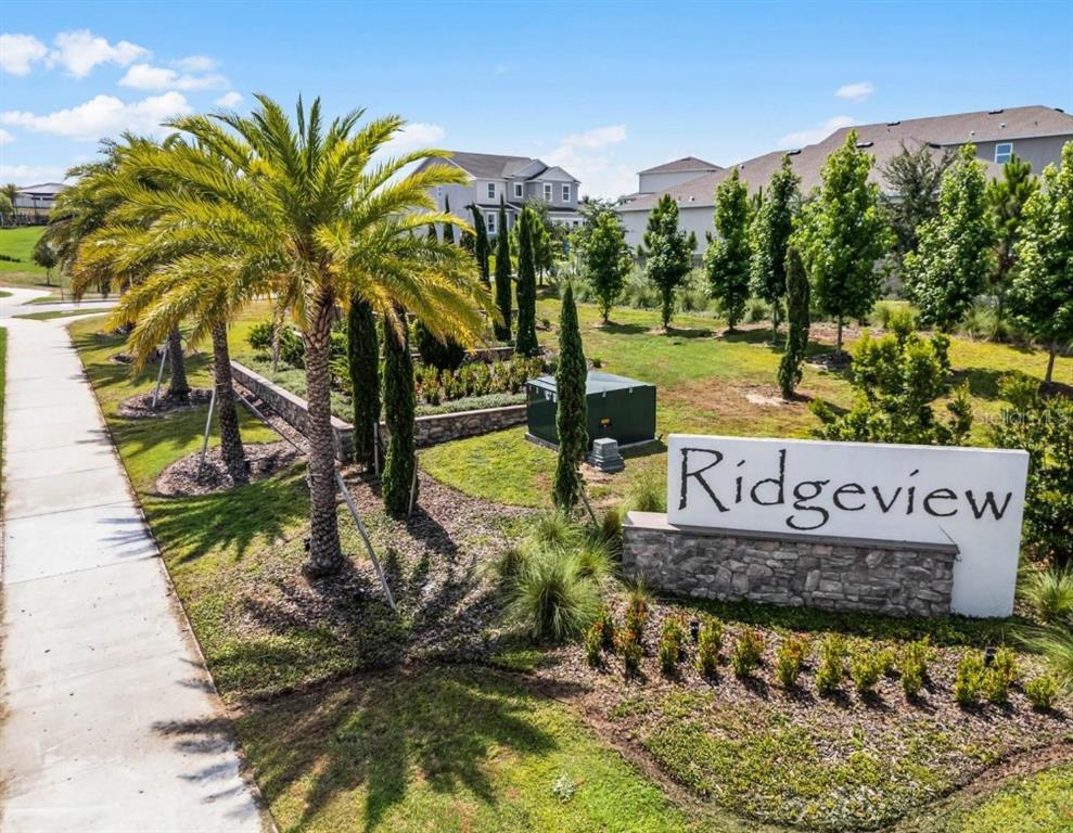 A stone-based sign reading Ridgeview stands near a sidewalk, palm trees, and residential houses — 14452 CRESTAVISTA AVENUE, CLERMONT, FL