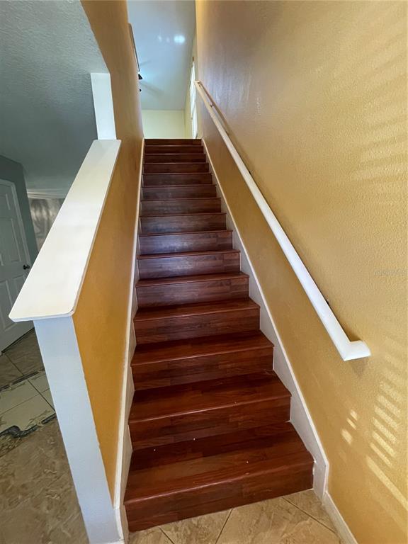 A wooden staircase with a white handrail ascends between yellow walls — 227 GLOWING PEACE LANE UNIT 83, ORLANDO, FL