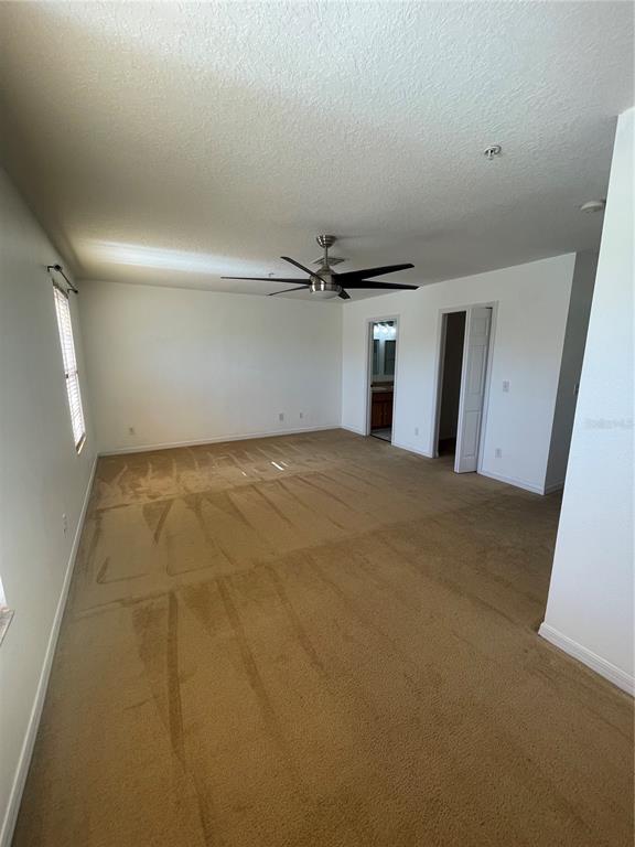 A spacious bedroom features beige carpeting, white walls, a ceiling fan, and two doorways — 227 GLOWING PEACE LANE UNIT 83, ORLANDO, FL