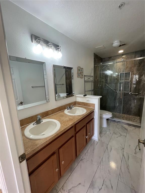 A bathroom features a double vanity with wood cabinets, two mirrors, and a glass-enclosed shower — 227 GLOWING PEACE LANE UNIT 83, ORLANDO, FL