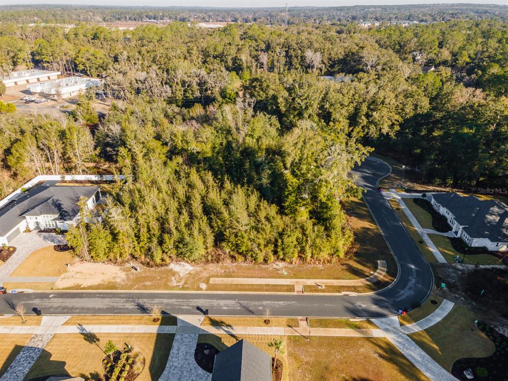 An aerial view shows a vacant, wooded residential lot situated between two houses on a street — 608 SW 139TH COURT, NEWBERRY, FL