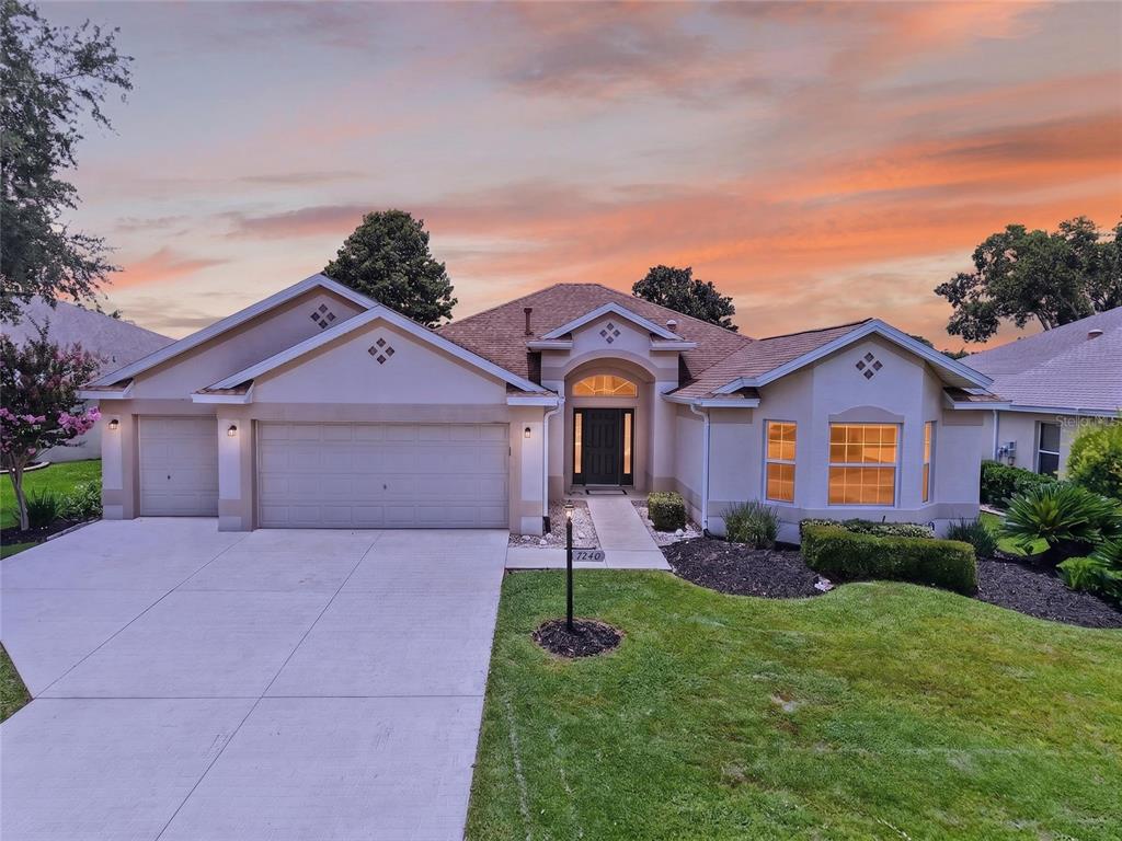 A single-story house with a three-car garage and a landscaped front yard at sunset — 7240 SE 172ND LEGACY LANE, THE VILLAGES, FL