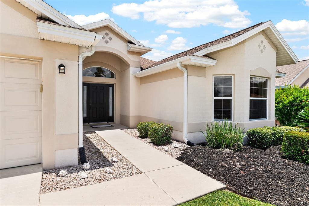 The exterior of a beige house features a front entrance, garage, and landscaped yard — 7240 SE 172ND LEGACY LANE, THE VILLAGES, FL