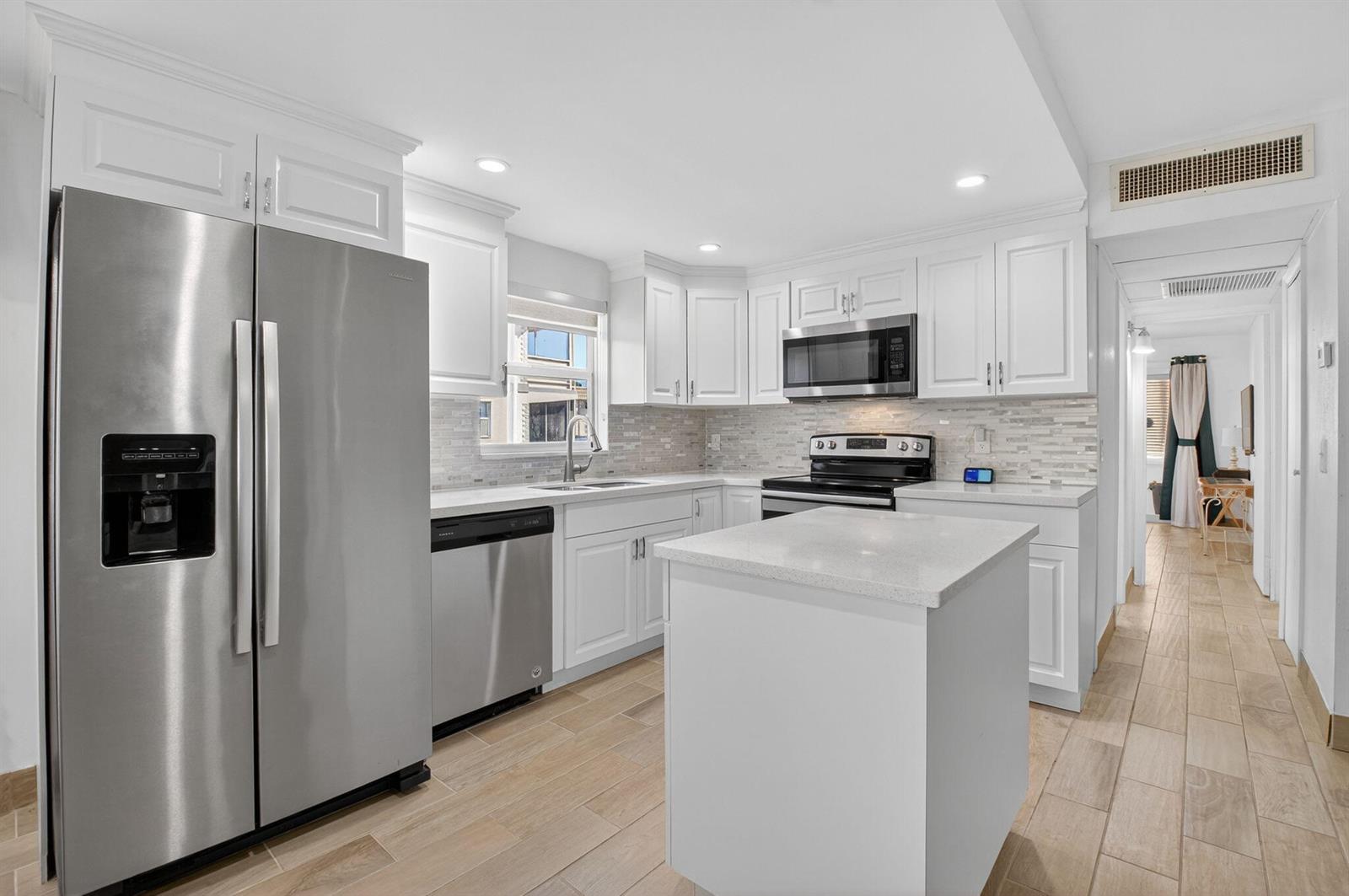 A kitchen with white cabinets, stainless steel appliances, a center island, and wood-look tile flooring — 60 Brittany # B, Delray Beach FL 33446, DELRAY BEACH, FL