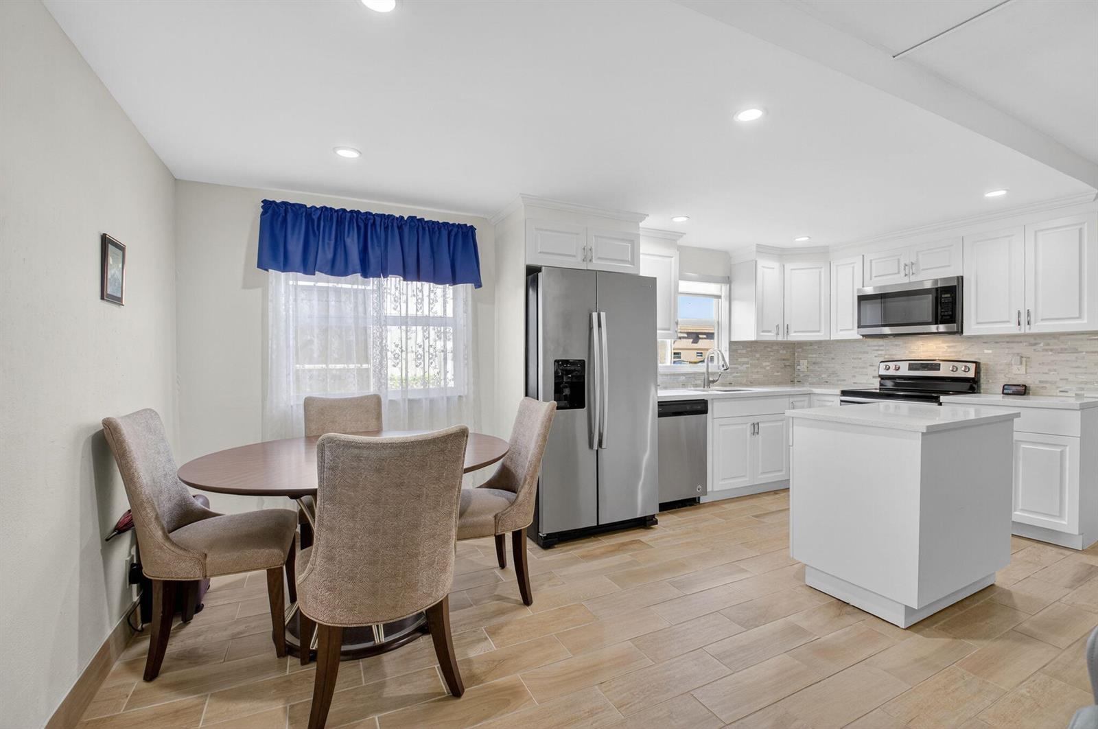 A kitchen and dining area with white cabinets, stainless steel appliances, and wood-look tile flooring — 60 Brittany # B, Delray Beach FL 33446, DELRAY BEACH, FL