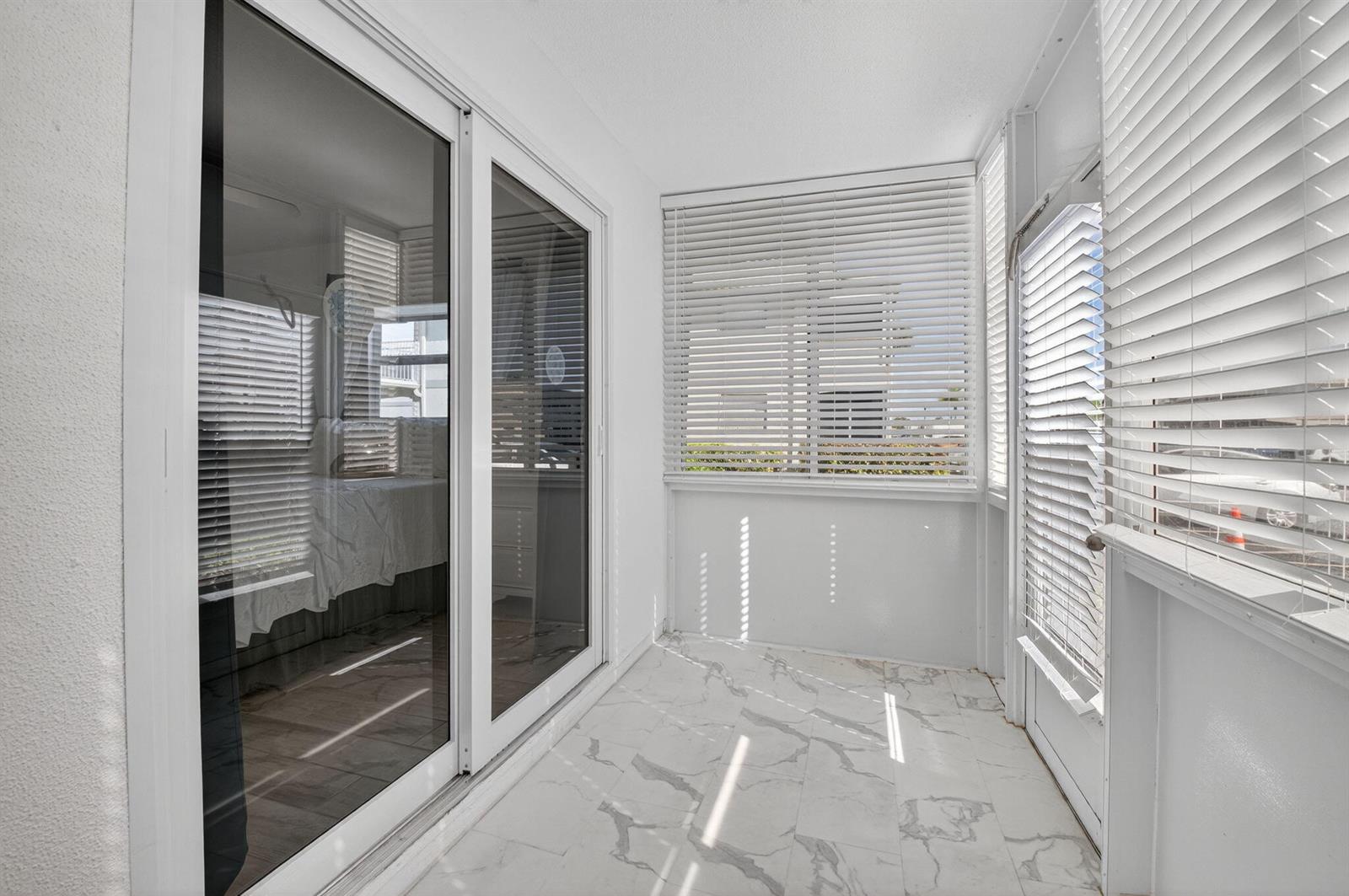 A sunroom with white walls, marble-look tile flooring, and large windows with horizontal blinds — 60 Brittany # B, Delray Beach FL 33446, DELRAY BEACH, FL