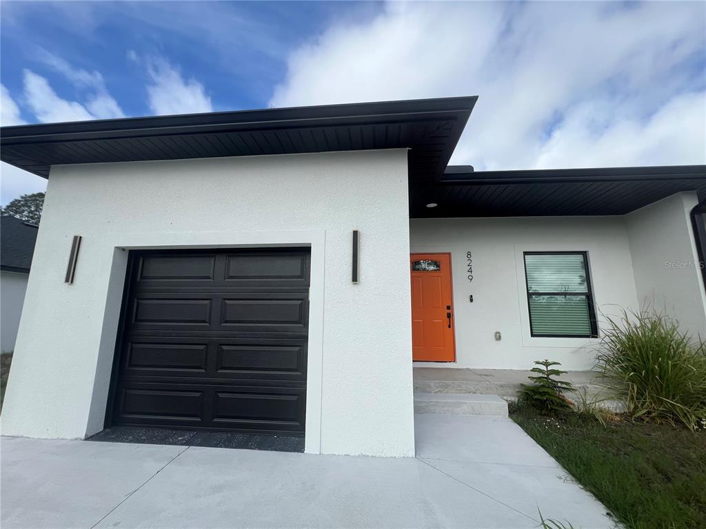 A modern white house exterior features a black garage door and a bright orange door — 8249 DIMSTEAD STREET, PORT CHARLOTTE, FL