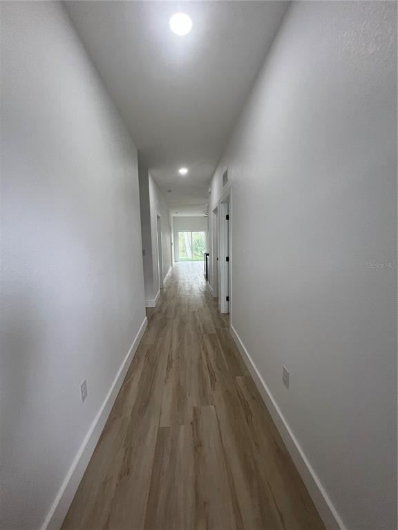 A long hallway with white walls and light wood-look flooring leads to a glass door — 8249 DIMSTEAD STREET, PORT CHARLOTTE, FL