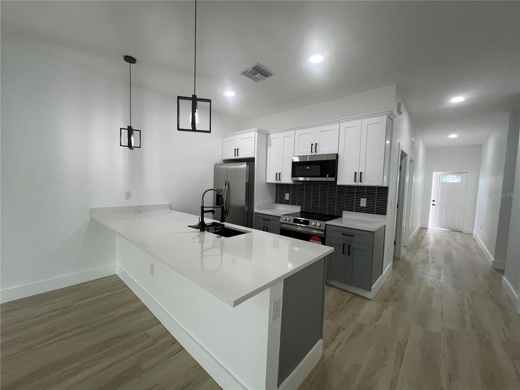 A modern kitchen features white upper cabinets, gray lower cabinets, and a white quartz island — 8249 DIMSTEAD STREET, PORT CHARLOTTE, FL