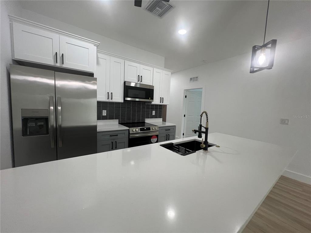 A modern kitchen features white upper cabinets, gray lower cabinets, and a large white island — 8249 DIMSTEAD STREET, PORT CHARLOTTE, FL
