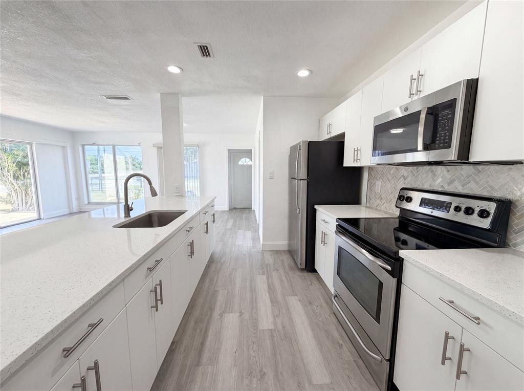 A modern kitchen features white cabinets, stainless steel appliances, and a large quartz island — 21530 GLENDALE AVENUE, PORT CHARLOTTE, FL