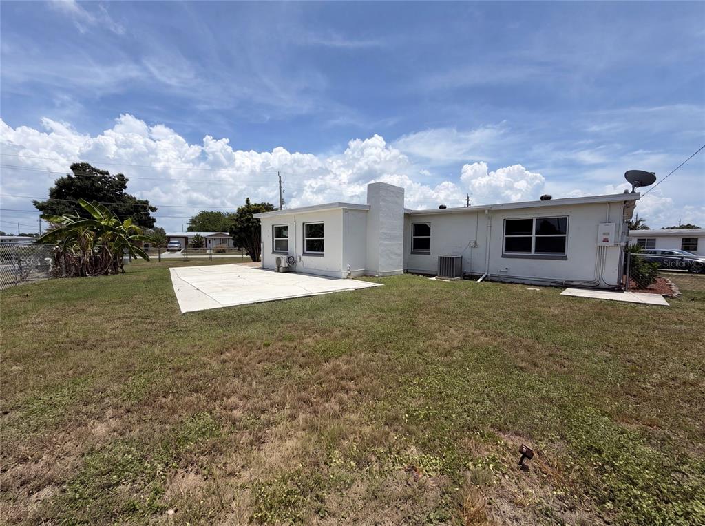 The exterior of a white, single-story house features a concrete patio and a grassy yard — 21530 GLENDALE AVENUE, PORT CHARLOTTE, FL