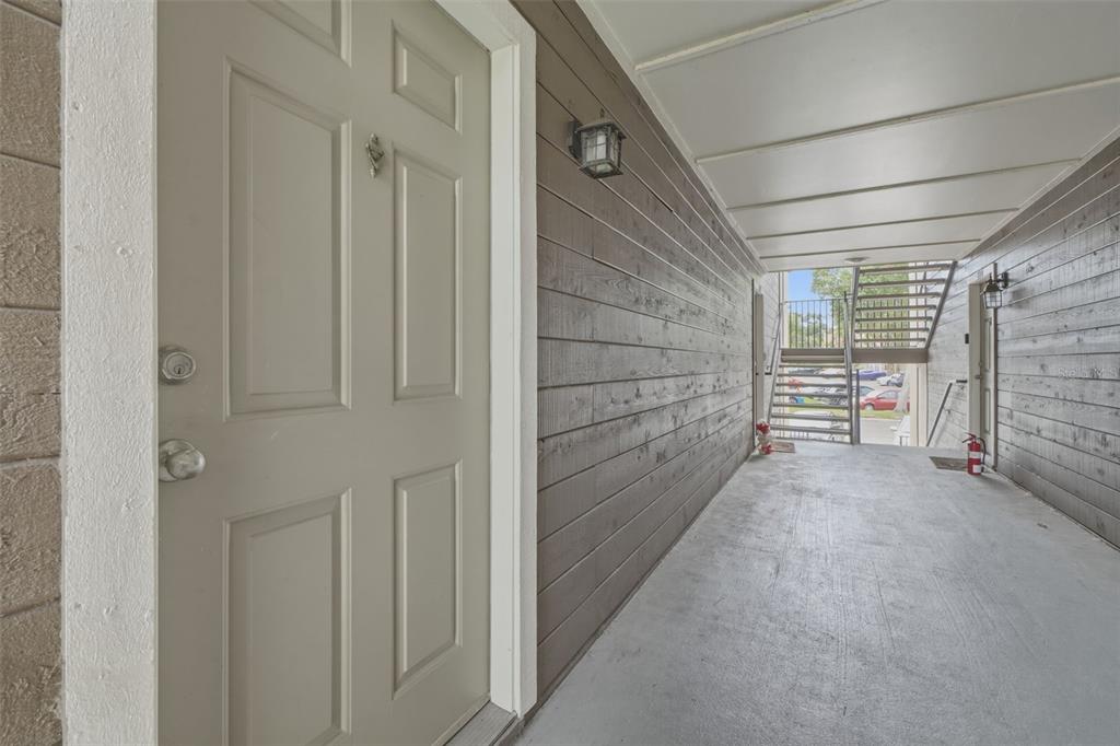 An exterior walkway with a light-colored door, wood-paneled walls, and a metal staircase — 249 AFTON SQUARE UNIT 208, ALTAMONTE SPRINGS, FL
