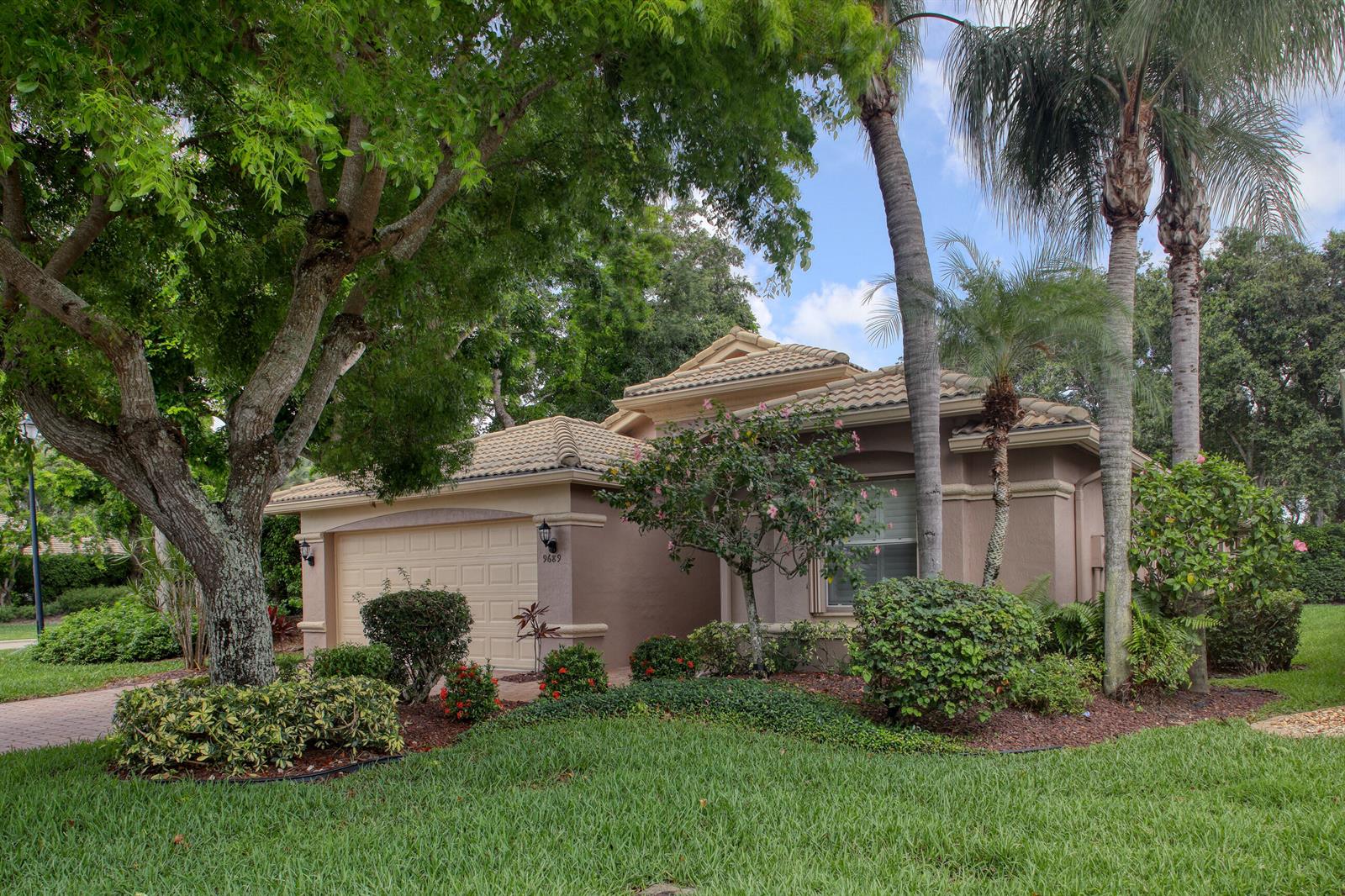 A single-story tan house with a tiled roof, a two-car garage, and lush landscaping — 9689 Positano Way, Lake Worth FL 33467, LAKE WORTH, FL