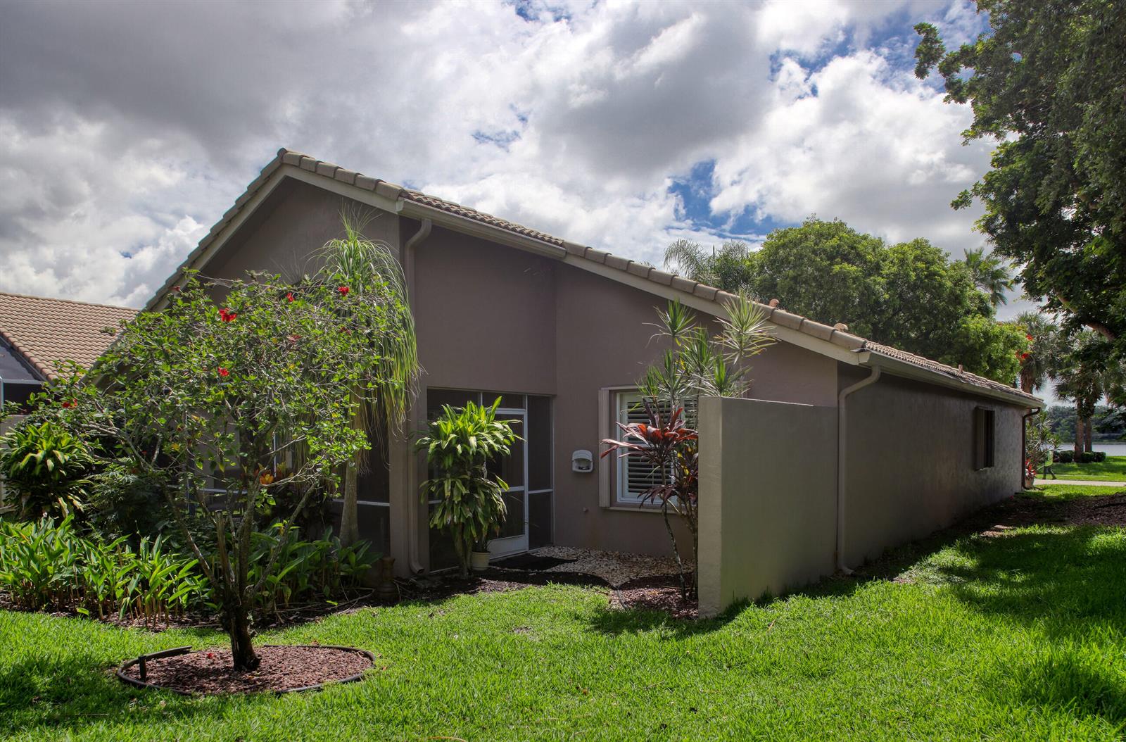 A tan single-story house with a screened-in porch and tropical landscaping under a cloudy sky — 9689 Positano Way, Lake Worth FL 33467, LAKE WORTH, FL
