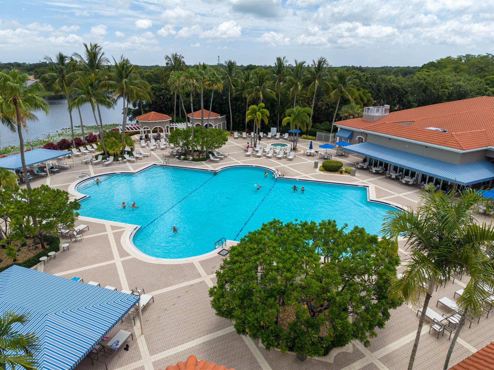 An aerial view shows a large swimming pool surrounded by a patio, palm trees, and buildings — 9689 Positano Way, Lake Worth FL 33467, LAKE WORTH, FL