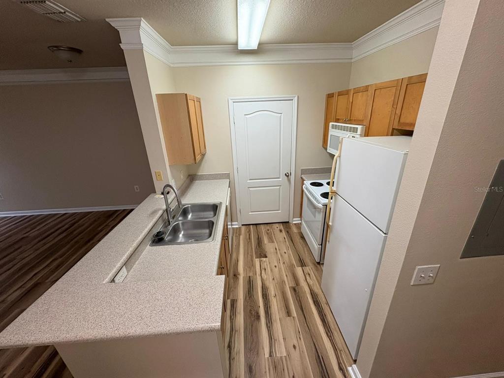 A kitchen features light-colored countertops, wood-look flooring, light wood cabinets, and white appliances — 8801 VILLA VIEW CIRCLE UNIT 206, ORLANDO, FL
