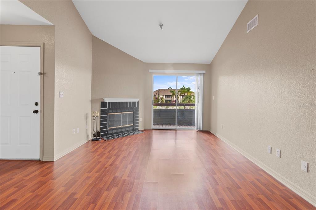 An empty living room features wood-look flooring, a corner fireplace, and a sliding glass door — 10265 GANDY BOULEVARD N UNIT 914, ST PETERSBURG, FL