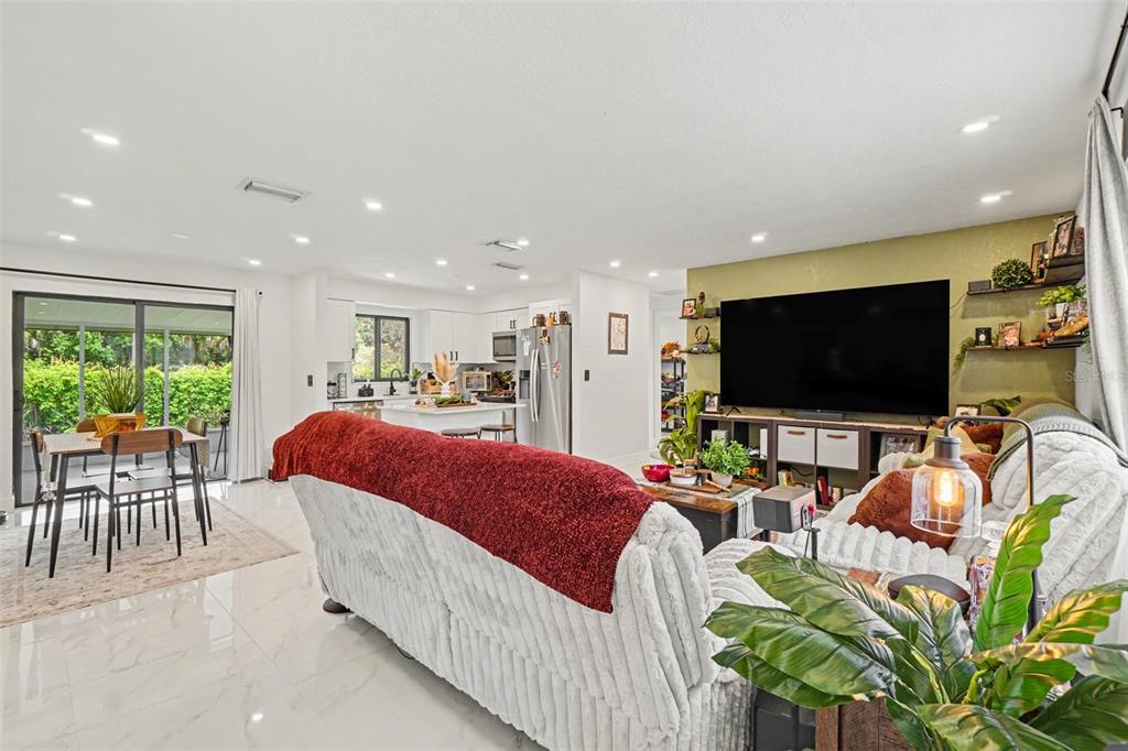 An open-concept living room and kitchen feature white tile floors, a large television, and sliding doors — 73 CARDINAL DRIVE, NORTH FORT MYERS, FL