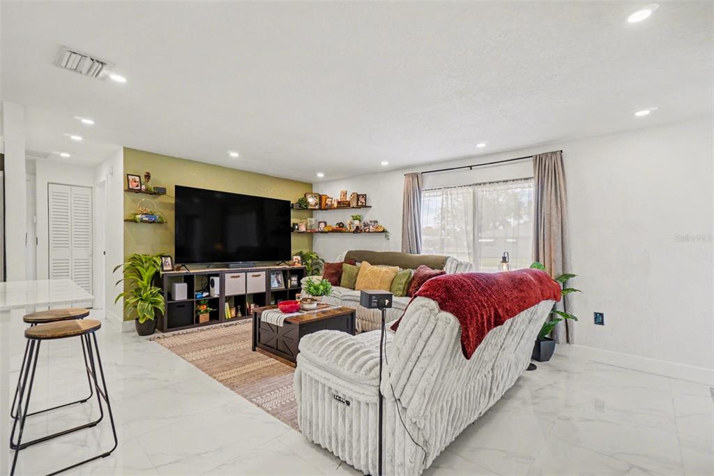 A living room features a large television, open shelving, a sectional sofa, and tiled floors — 73 CARDINAL DRIVE, NORTH FORT MYERS, FL
