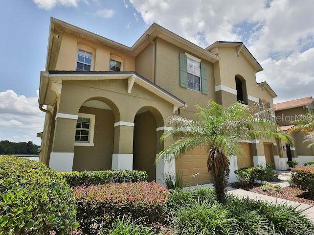 A two-story tan house with a covered entryway and a palm tree in the front yard — 3893 GLIDING PLACE, SANFORD, FL
