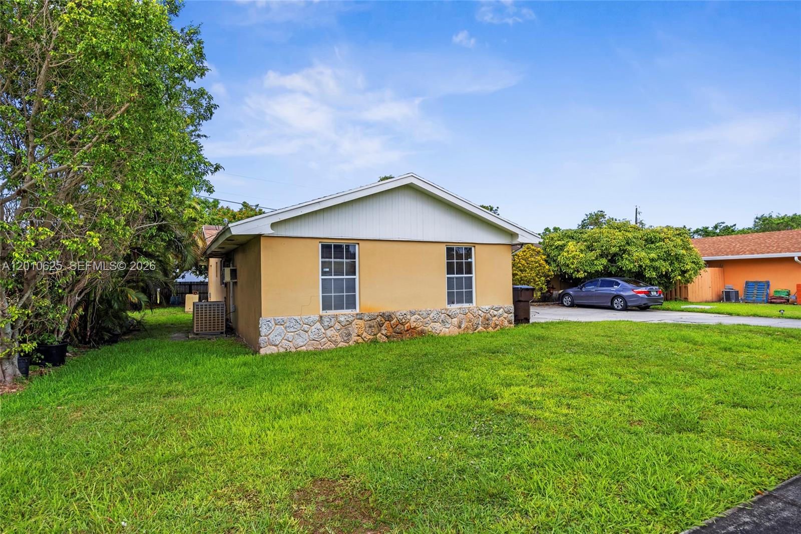 A single-story house with a stone-veneer base and yellow siding sits on a grassy lot — 1831 Hiltonia Cir, West Palm Beach FL 33407, WEST PALM BEACH, FL