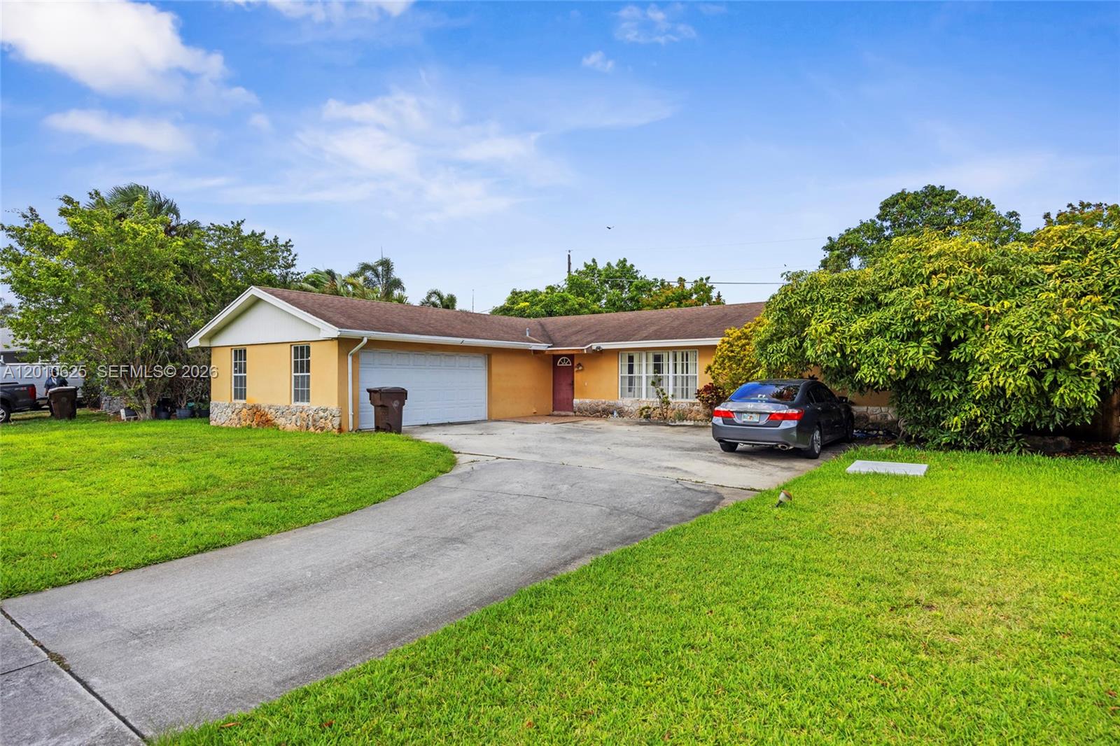 A single-story house with a yellow exterior, stone accents, a garage, and a concrete driveway — 1831 Hiltonia Cir, West Palm Beach FL 33407, WEST PALM BEACH, FL