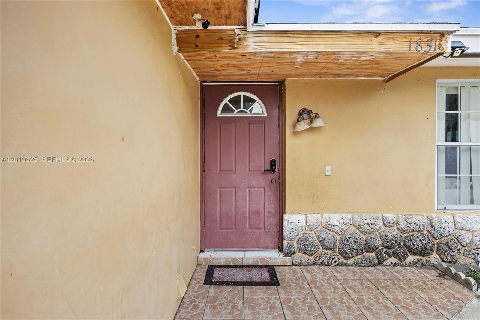 The exterior entrance features a maroon door, stone siding, and a wood-paneled porch ceiling — 1831 Hiltonia Cir, West Palm Beach FL 33407, WEST PALM BEACH, FL