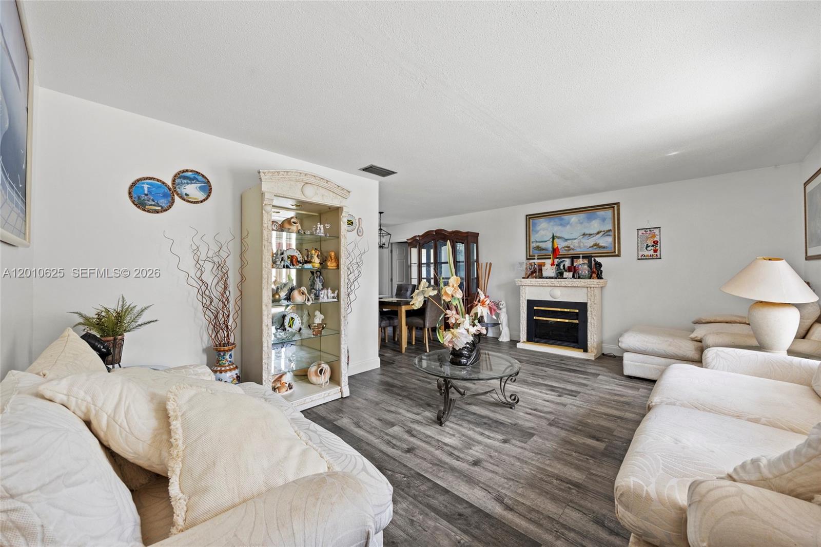 A living room features a fireplace, a glass display cabinet, and light-colored sofas on wood-look flooring — 1831 Hiltonia Cir, West Palm Beach FL 33407, WEST PALM BEACH, FL