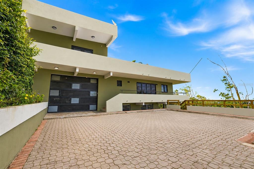 A modern, multi-level olive green house with a paved driveway and a large garage door — RD15 KM20.6 BO. QUEBRADA ARRIBA, CAYEY, PR
