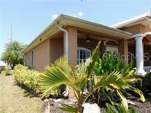 A tan stucco house features a covered front porch with a white column and landscaping — 25352 DOREDO DRIVE, PUNTA GORDA, FL