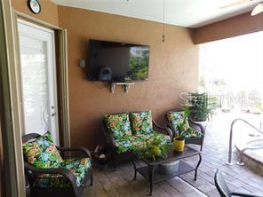 A covered patio features wicker furniture with floral cushions, a wall-mounted television, and tile flooring — 25352 DOREDO DRIVE, PUNTA GORDA, FL