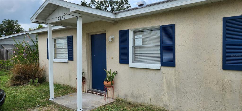 A single-story house exterior features beige stucco walls, blue shutters, and a small covered porch — 9831 GRACE DRIVE, PORT RICHEY, FL