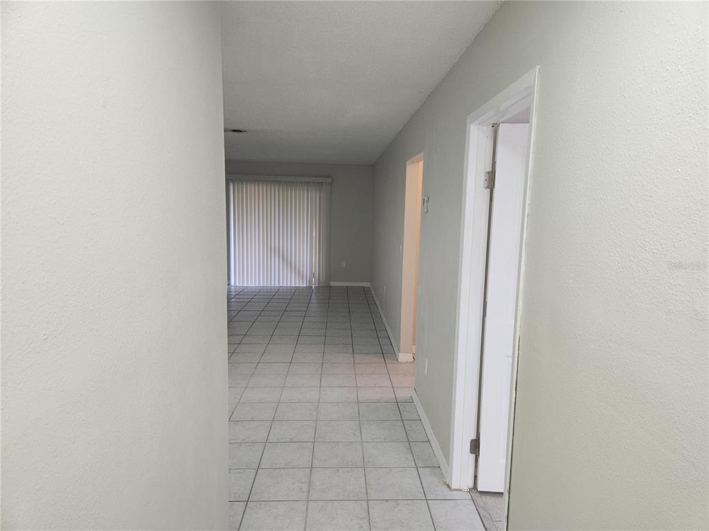 A hallway with light-colored tile flooring leads toward a living area with vertical blinds — 9831 GRACE DRIVE, PORT RICHEY, FL