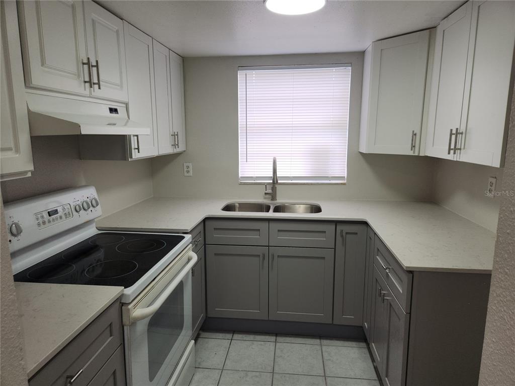 A kitchen features white upper cabinets, gray lower cabinets, a white stove, and light countertops — 9831 GRACE DRIVE, PORT RICHEY, FL