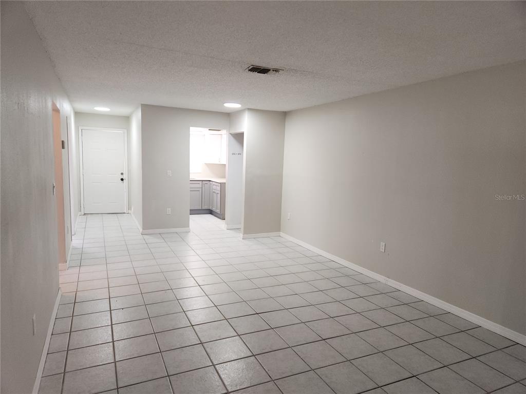 An open-concept living area features light-colored tile flooring, gray walls, and a view into a kitchen — 9831 GRACE DRIVE, PORT RICHEY, FL