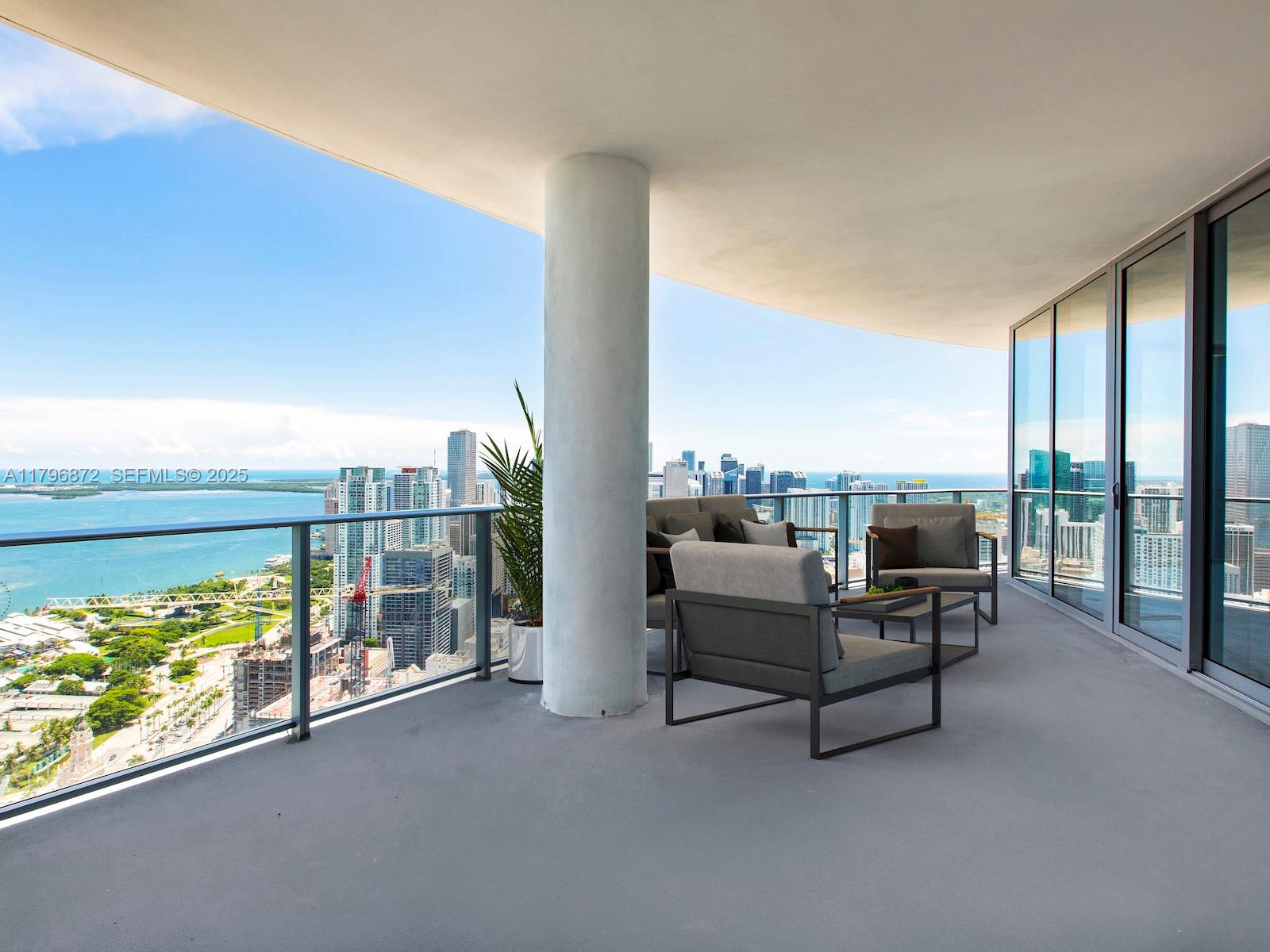 A high-rise balcony features outdoor seating, a central support column, and panoramic city and water views — 851 NE 1st Ave, Miami FL 33132, MIAMI, FL