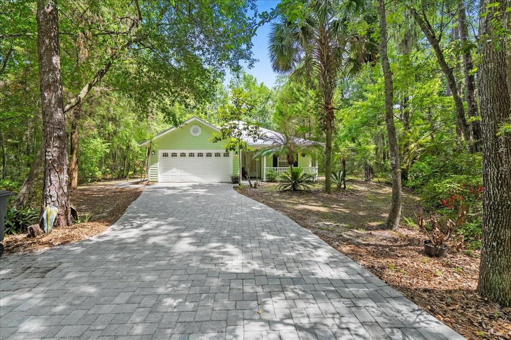 A light green house with a white garage door and a paved driveway in a forest — 5526 DON MANUEL ROAD, ELKTON, FL