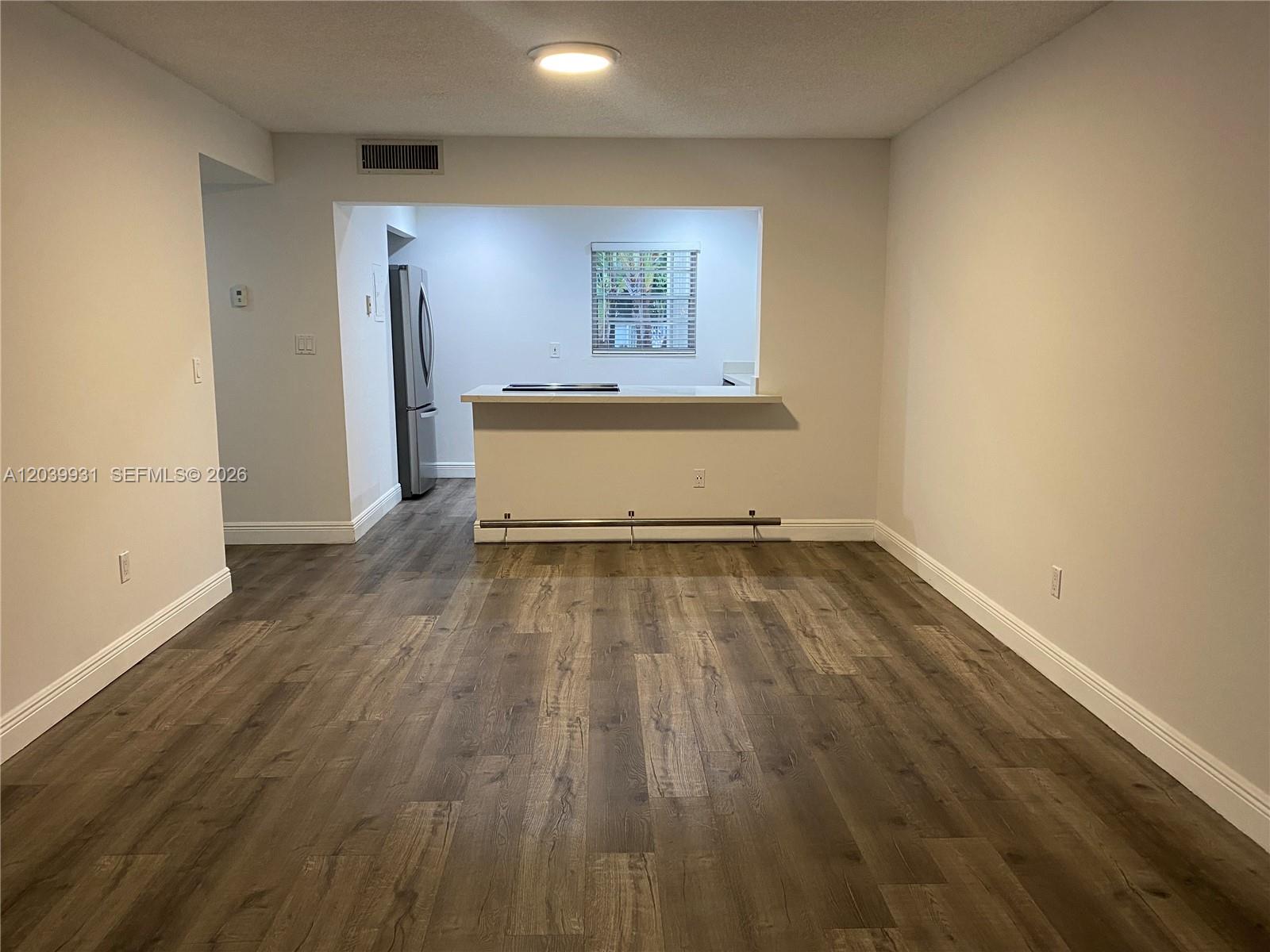 A living area with wood-look flooring opens to a kitchen with a breakfast bar — 7755 SW 86th St # 107, Miami FL 33143, MIAMI, FL