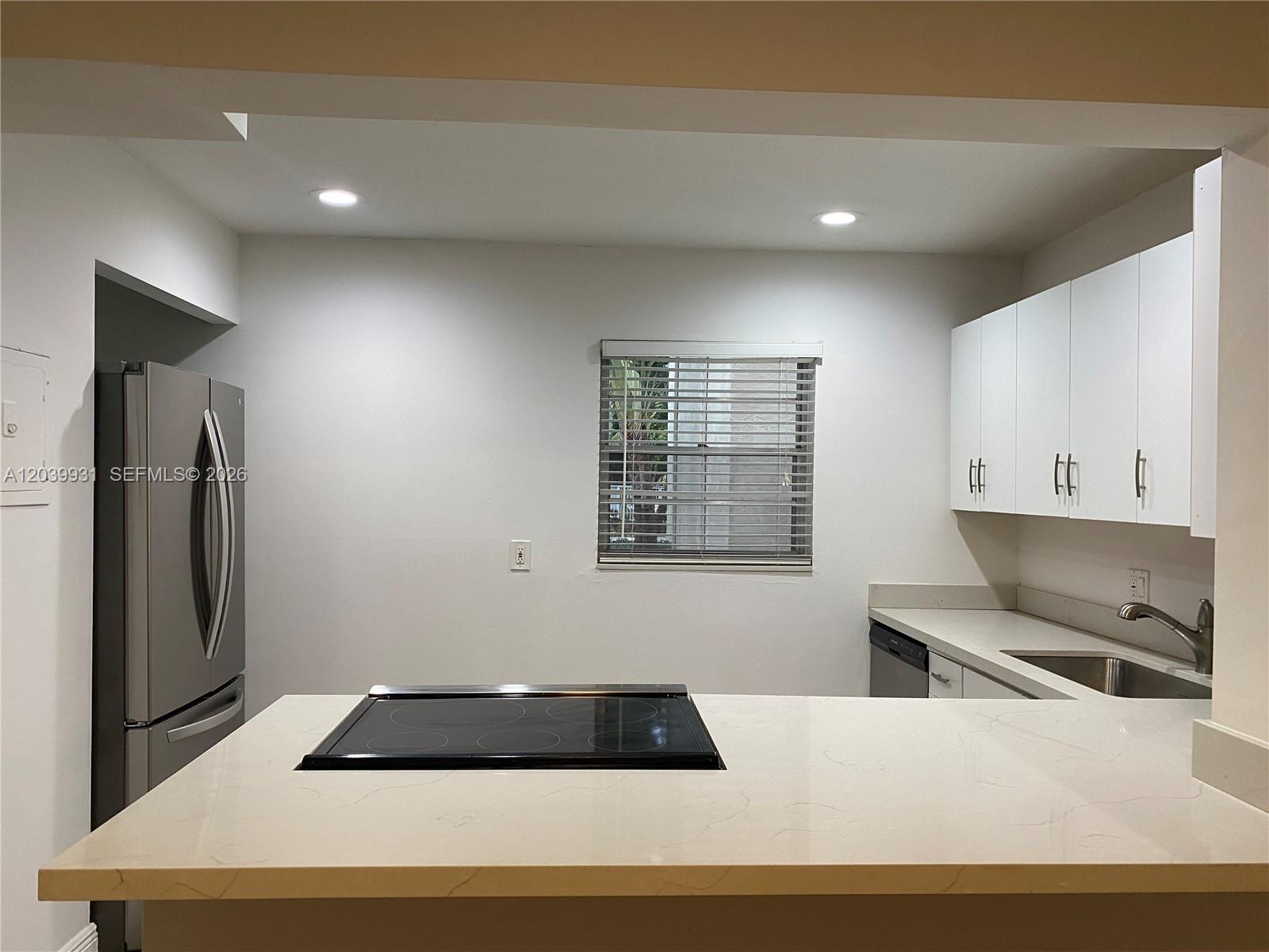 A kitchen features white cabinets, a stainless steel refrigerator, and a cooktop on the island — 7755 SW 86th St # 107, Miami FL 33143, MIAMI, FL