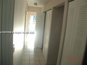 A hallway with white tile flooring leads toward a doorway with natural light — 1318 White Pine Dr, Wellington FL 33414, WELLINGTON, FL