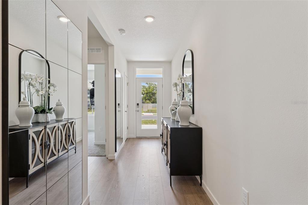 A bright entryway features light wood flooring, a mirrored wall, and two black console tables — 5115 NICKERBEAN STREET, APOPKA, FL