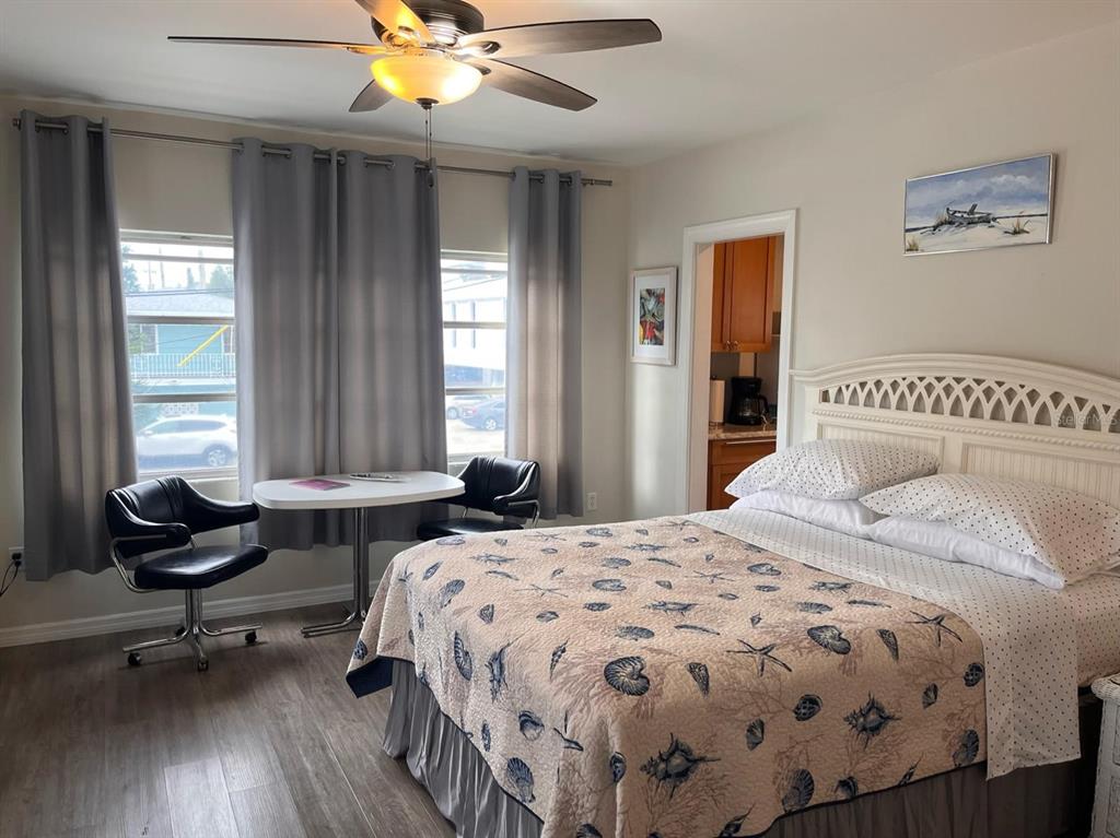 A bedroom features a bed with a seashell quilt, a small dining table, and gray curtains — 1901 HYDE PARK ST UNIT G, SARASOTA, FL