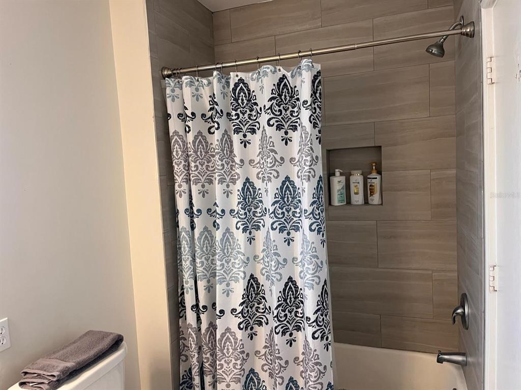 A bathroom features a tiled shower surround with a patterned curtain and a recessed niche — 1901 HYDE PARK ST UNIT G, SARASOTA, FL