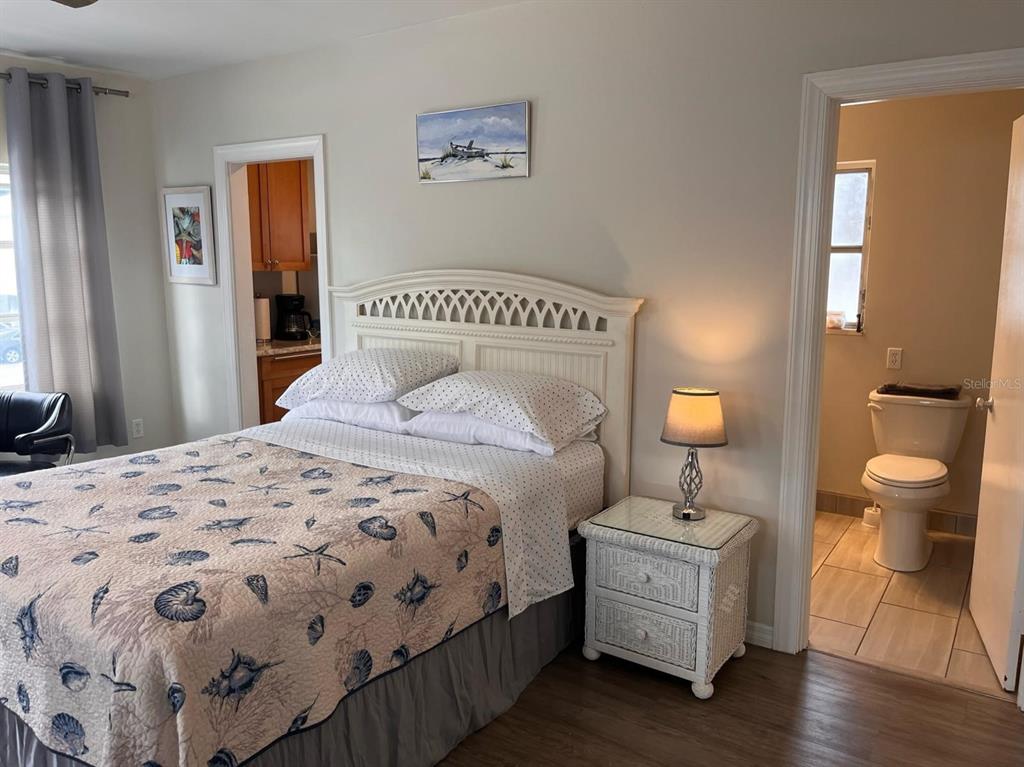 A bedroom with a seashell-patterned quilt, white headboard, wicker nightstand, and an attached bathroom — 1901 HYDE PARK ST UNIT G, SARASOTA, FL